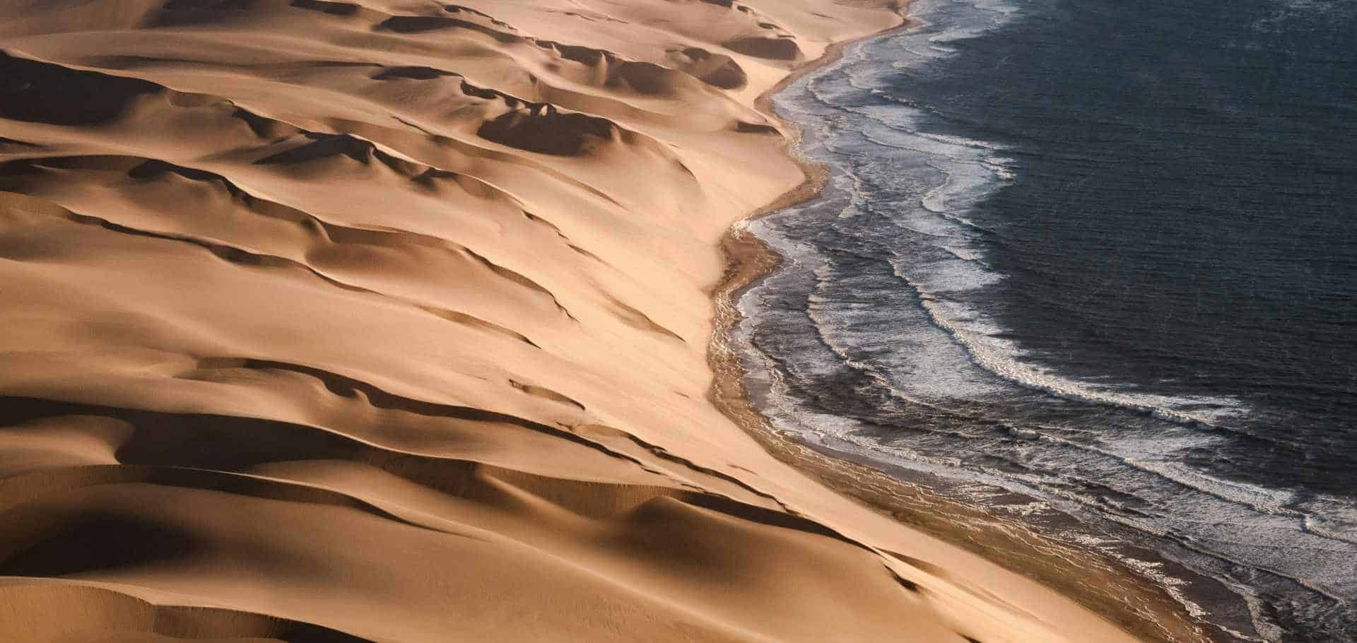 Aerial view of dramatic sand dunes plunging straight into the rough Atlantic Ocean.