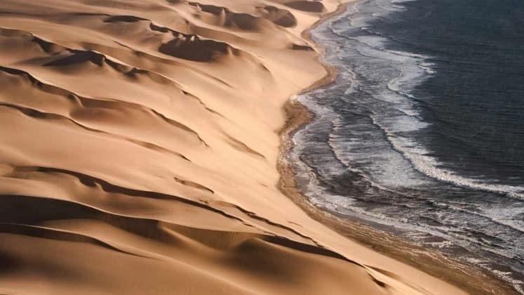 Aerial view of dramatic sand dunes plunging straight into the rough Atlantic Ocean.