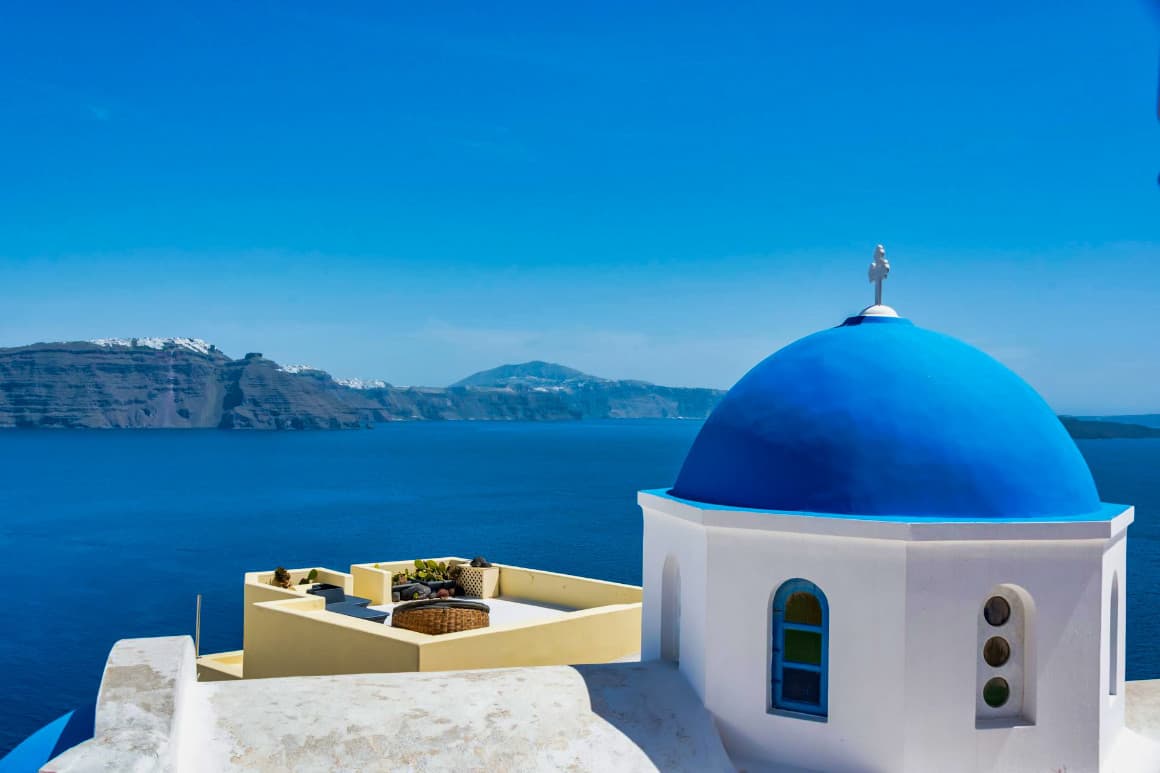 Famous blue dome of a Greek Orthodox church with a scenic view of the Aegean Sea in Santorini.