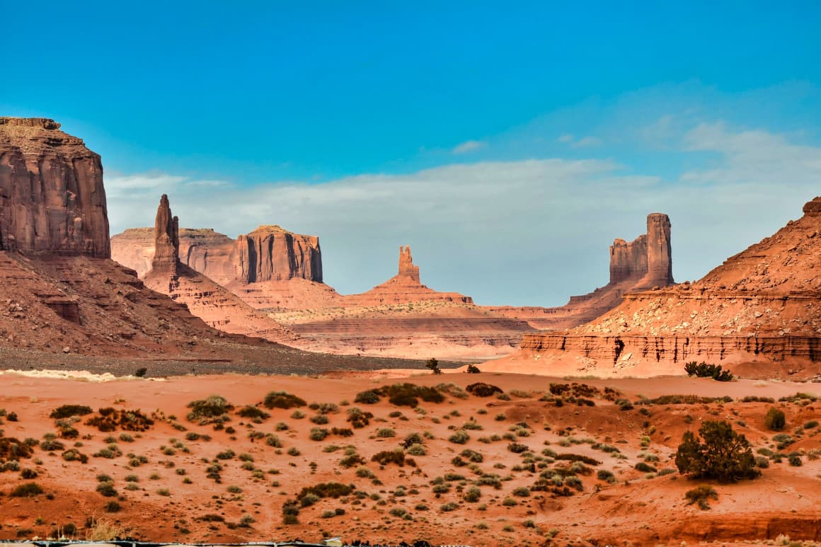 Dramatic desert landscape featuring iconic rock formations and red sand in Monument Valley.