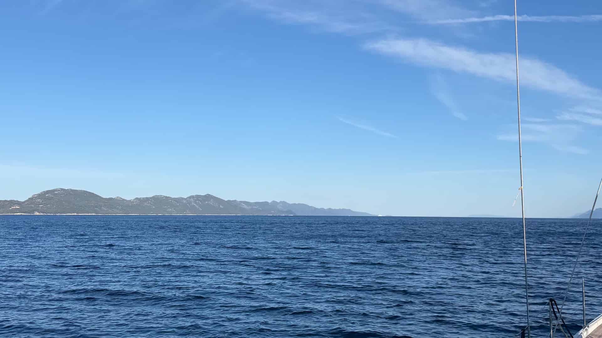 Wide view of blue sea water and distant hills framed by sailboat rigging.
