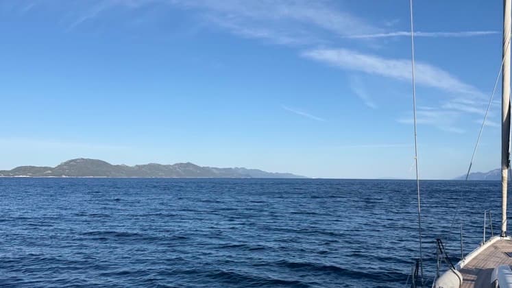 Wide view of blue sea water and distant hills framed by sailboat rigging.