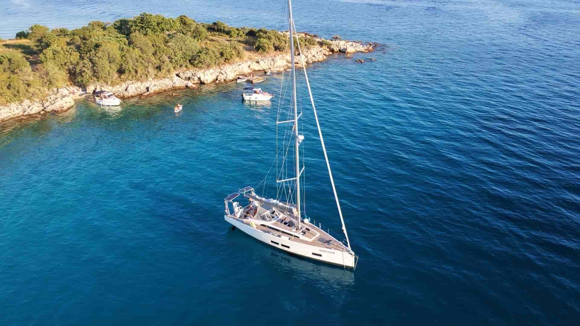 Modern monohull sailboat anchored in deep blue waters near the sunlit limestone coast of Sveti Juraj.