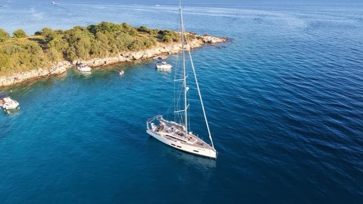 Modern monohull sailboat anchored in deep blue waters near the sunlit limestone coast of Sveti Juraj.