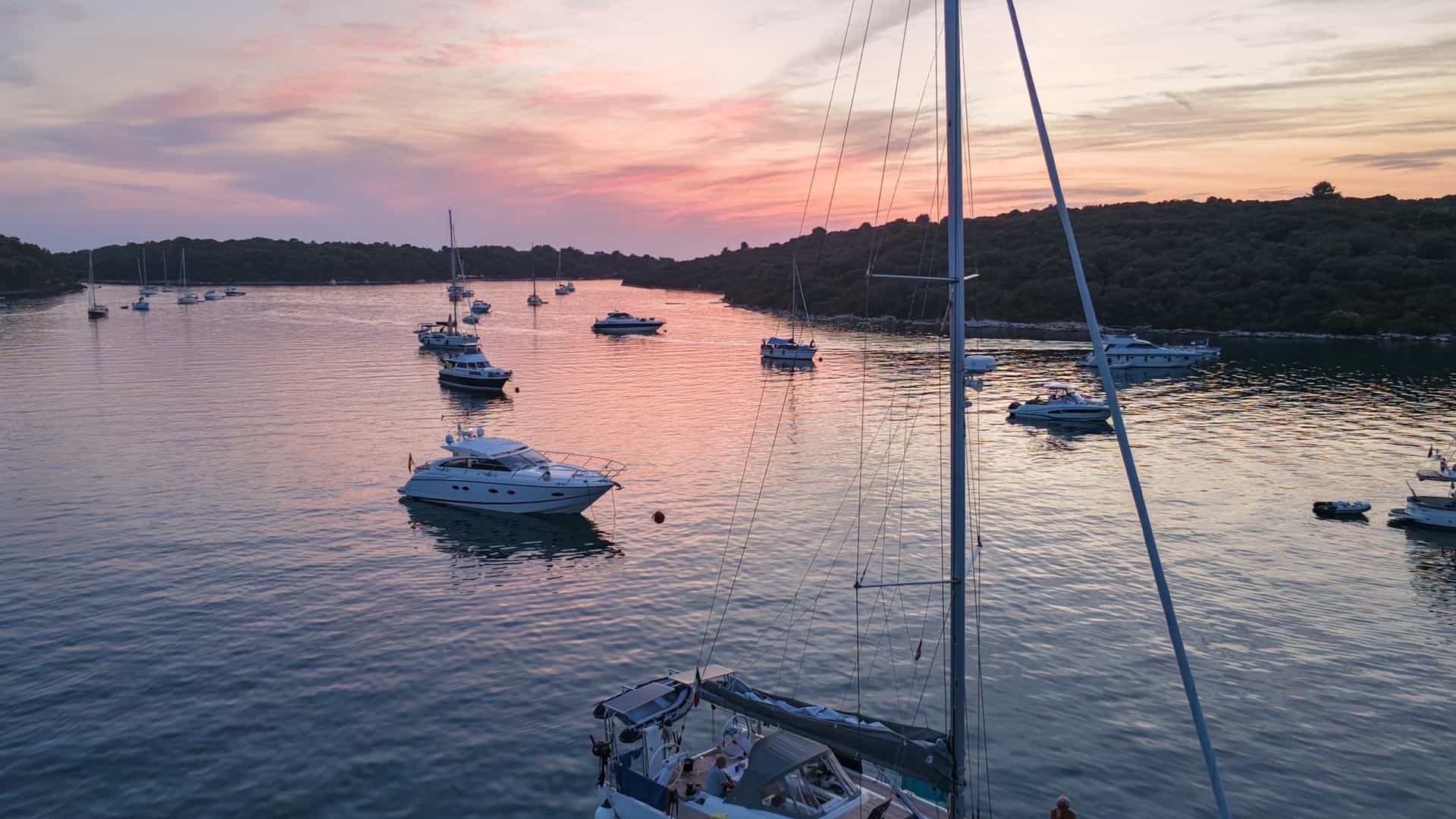 Sailboat cockpit view looking across Uvala Soline bay filled with yachts at golden hour.