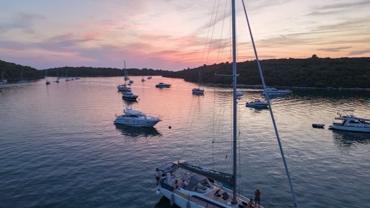 Sailboat cockpit view looking across Uvala Soline bay filled with yachts at golden hour.