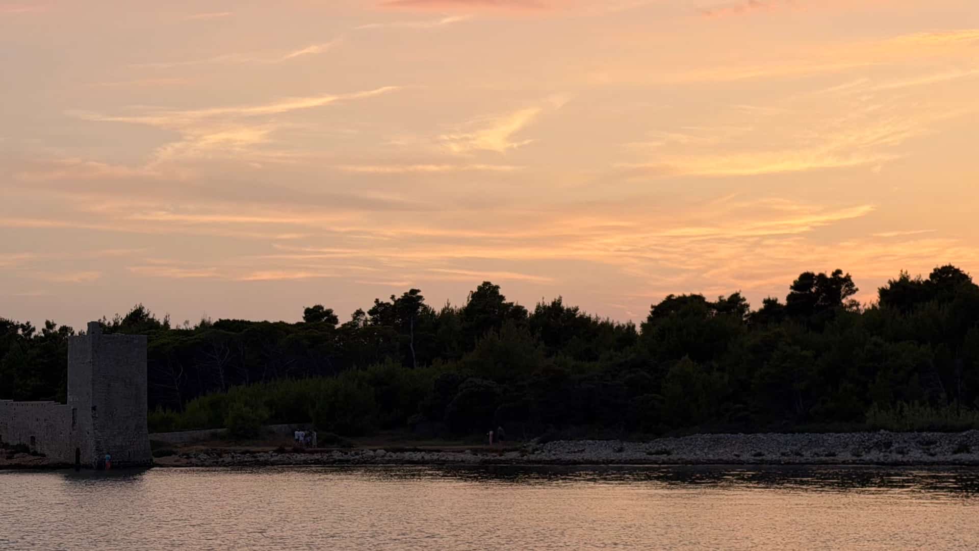 Distant profile of Kaštelina Castle's stone walls and towers standing on the intertidal shore at dusk.