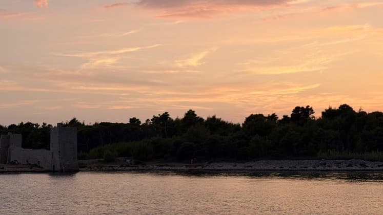 Distant profile of Kaštelina Castle's stone walls and towers standing on the intertidal shore at dusk.