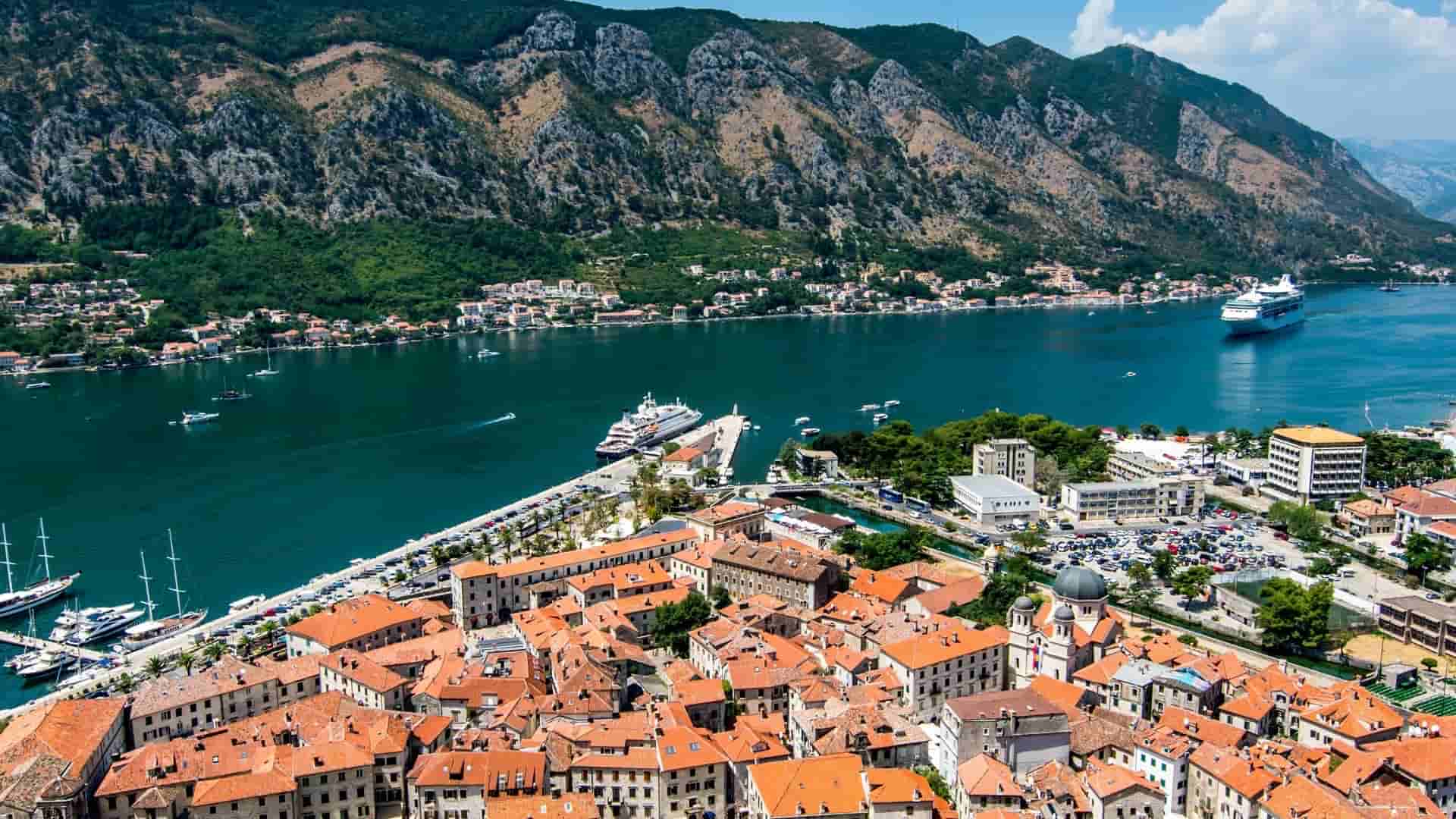Aerial view of Kotor red tile roofs beside blue bay water and rugged mountains.