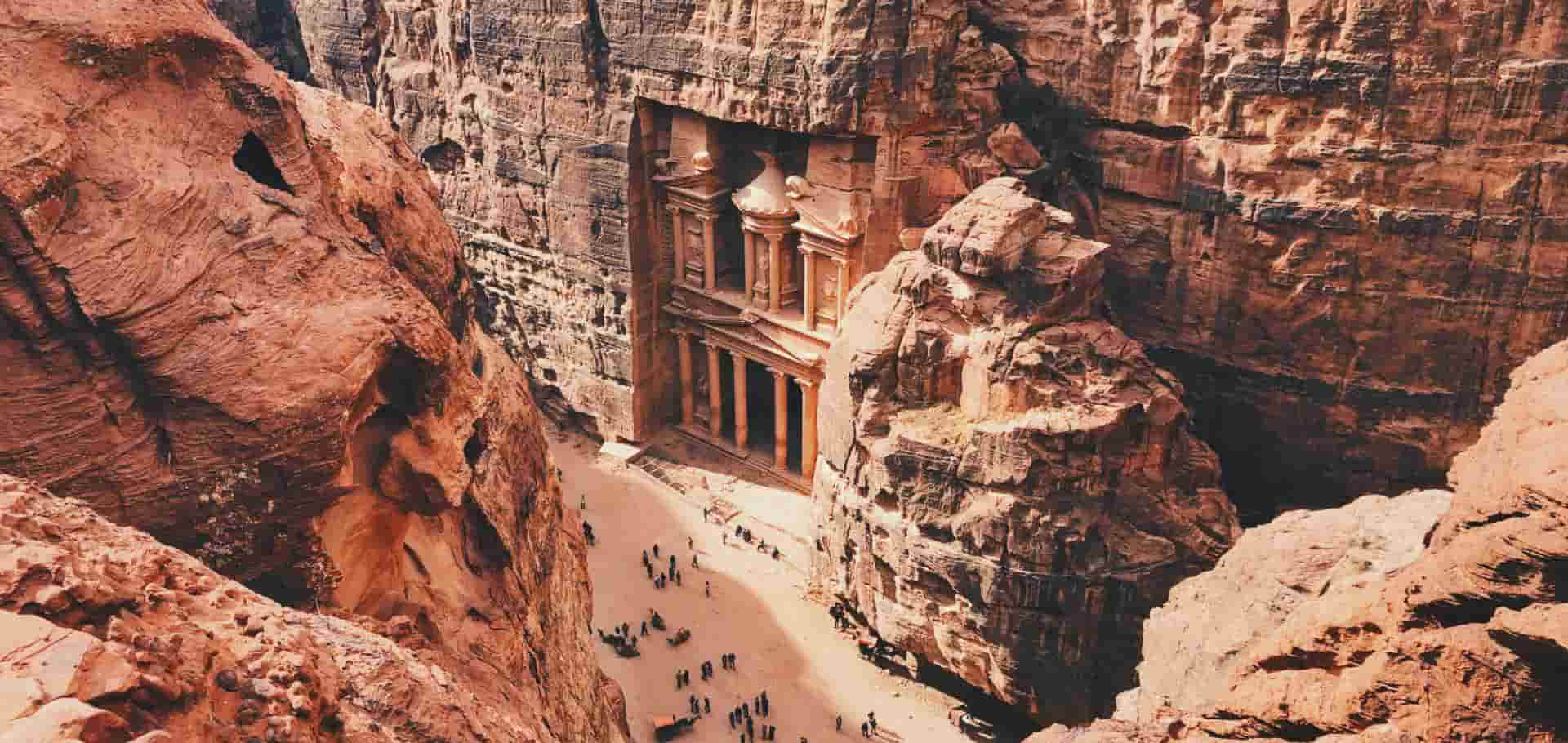 Visitors walking along the sandy canyon floor leading toward the magnificent Al-Khazneh facade in Petra