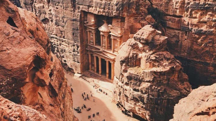 Visitors walking along the sandy canyon floor leading toward the magnificent Al-Khazneh facade in Petra
