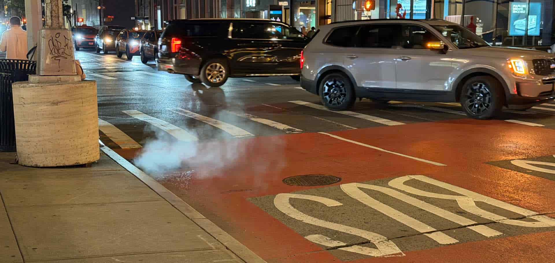 White steam plume rising from a street manhole cover near a bus lane in Manhattan