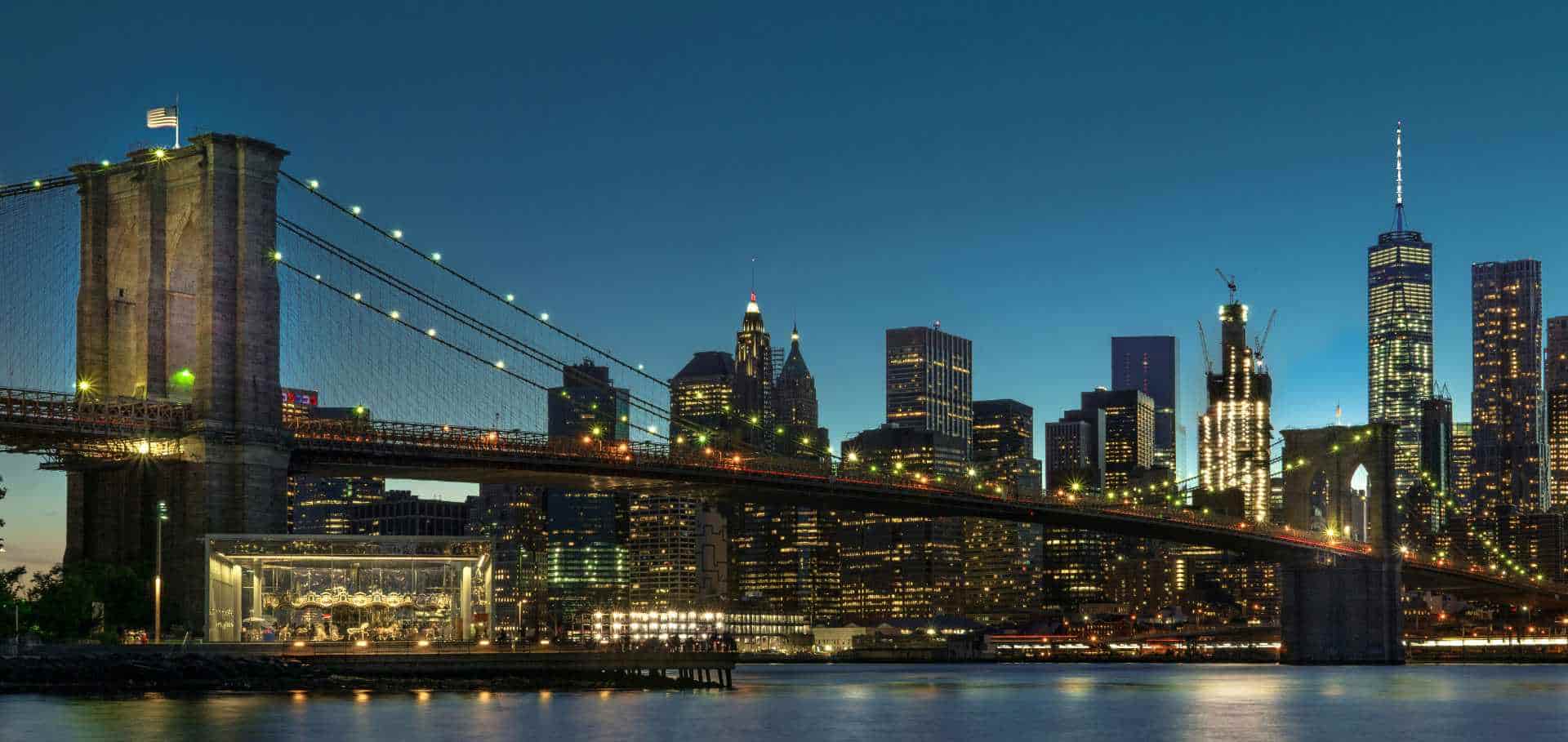 Evening illumination of the Brooklyn Bridge and the glowing skyscrapers of the Manhattan financial district.