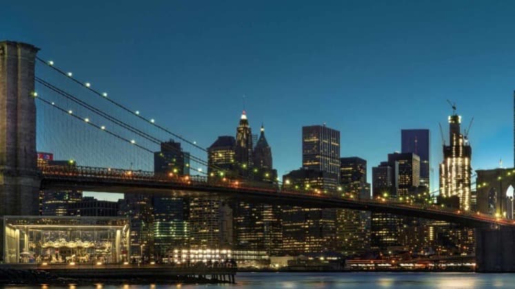 Evening illumination of the Brooklyn Bridge and the glowing skyscrapers of the Manhattan financial district.