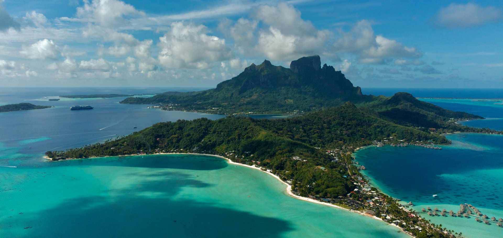 Aerial view of Bora Bora's iconic Mount Otemanu rising above turquoise lagoons and white sand beaches.