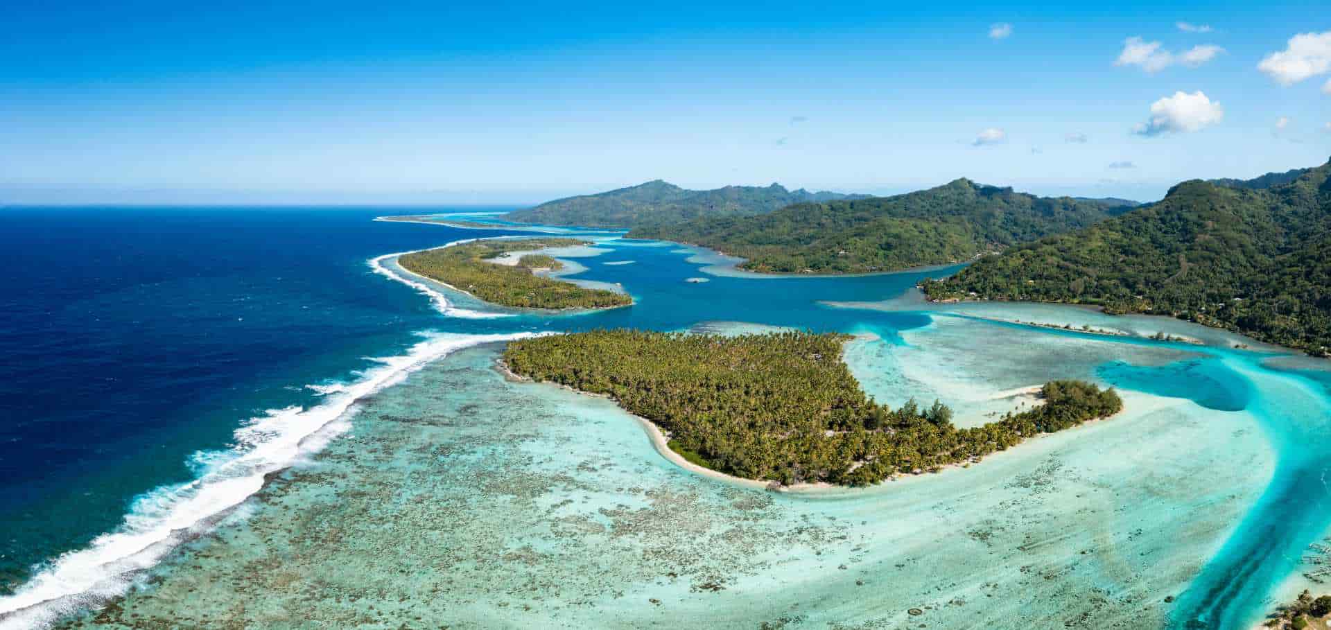 Aerial view of lush volcanic islands surrounded by turquoise lagoons and barrier reefs.