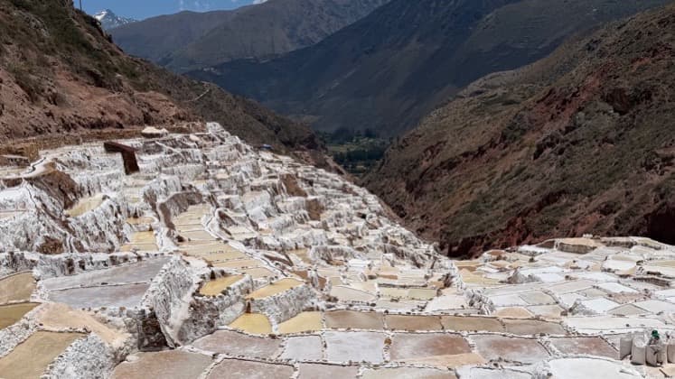 Cascading white salt evaporation ponds step down the red canyon slope in Peru.