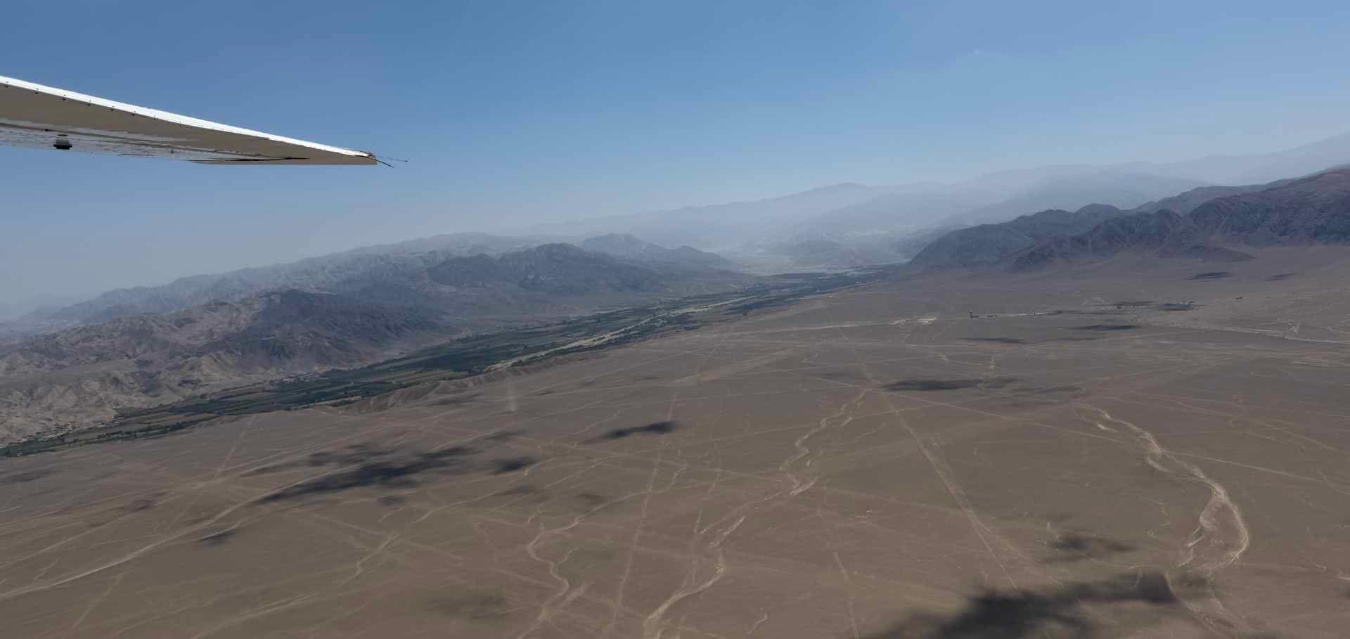 Aerial view of vast red iron-oxide desert plains crossed by ancient Nazca Line geoglyphs.
