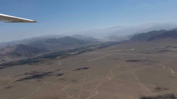 Aerial view of vast red iron-oxide desert plains crossed by ancient Nazca Line geoglyphs.