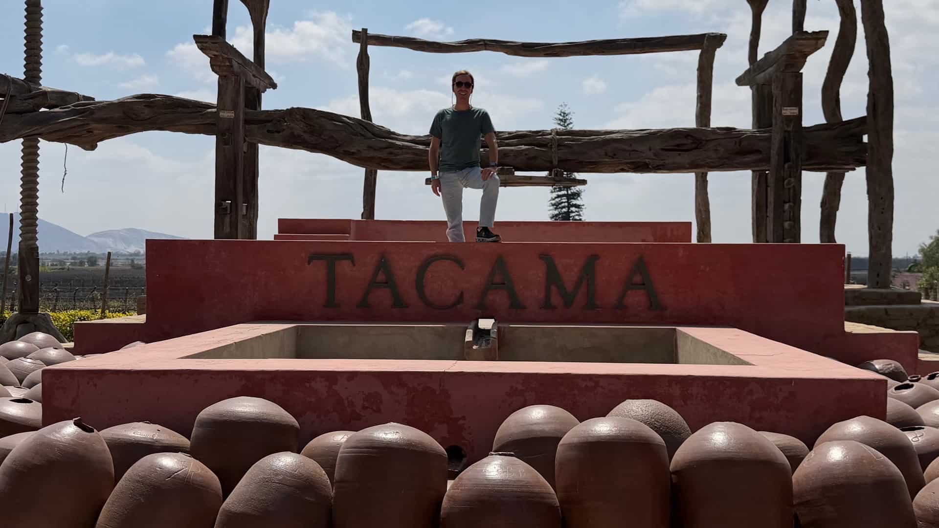 Traditional wooden wine press monument with clay jars and distant mountains at Tacama winery.