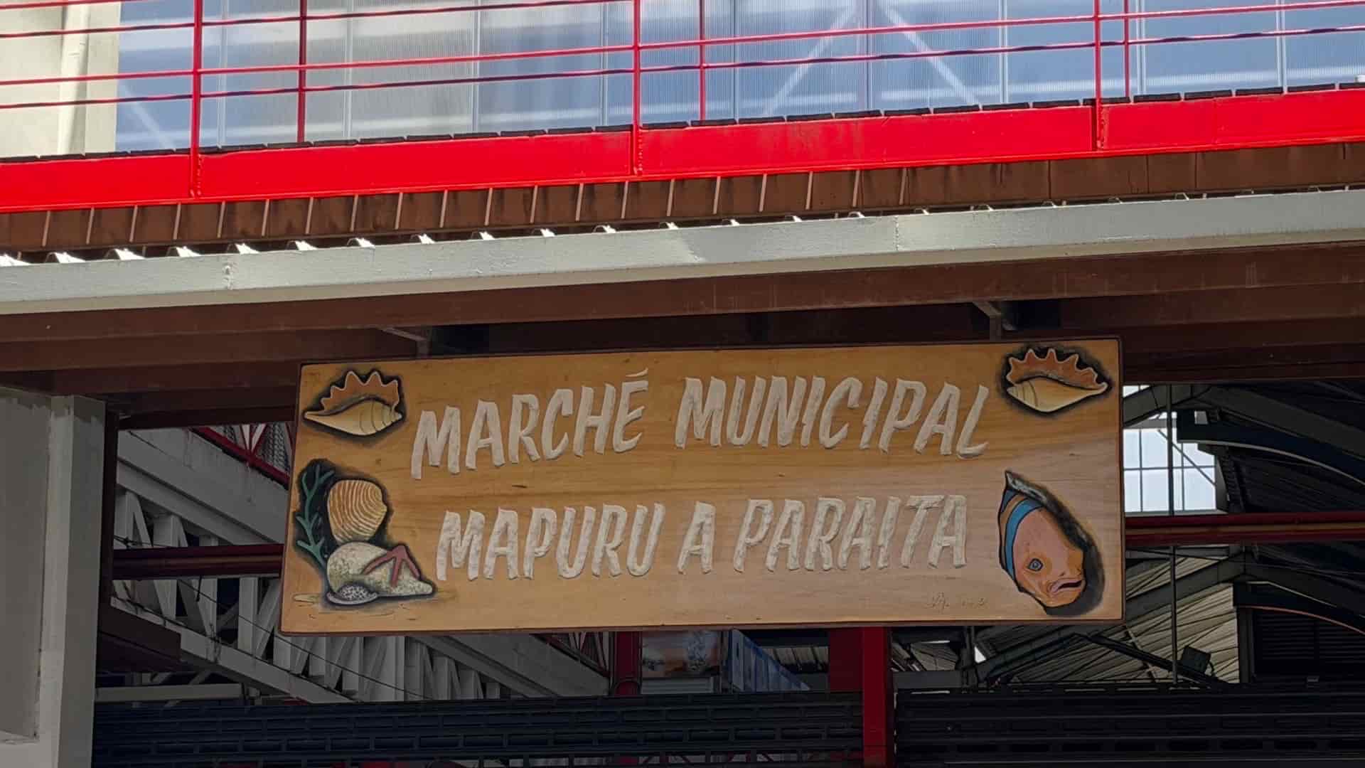 Wooden sign reading Marché Municipal Mapuru a Paraita adorned with decorative seashell carvings.