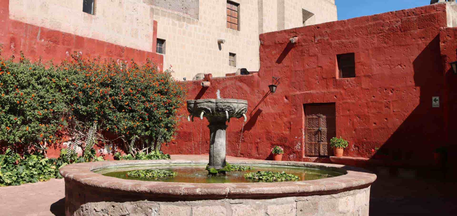 Stone fountain in a vibrant crimson courtyard surrounded by flowering plants in Santa Catalina.