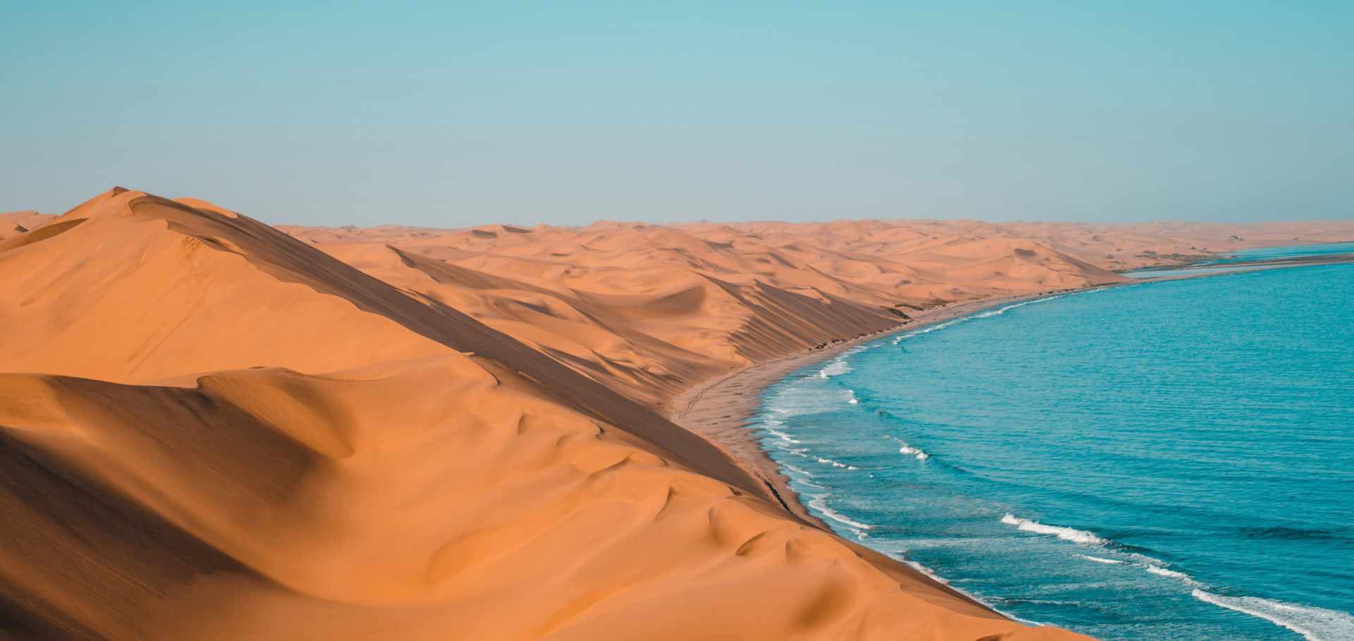Massive red sand dunes sweeping down to meet the blue ocean waters of the Namib coast