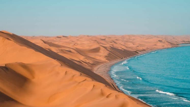 Massive red sand dunes sweeping down to meet the blue ocean waters of the Namib coast