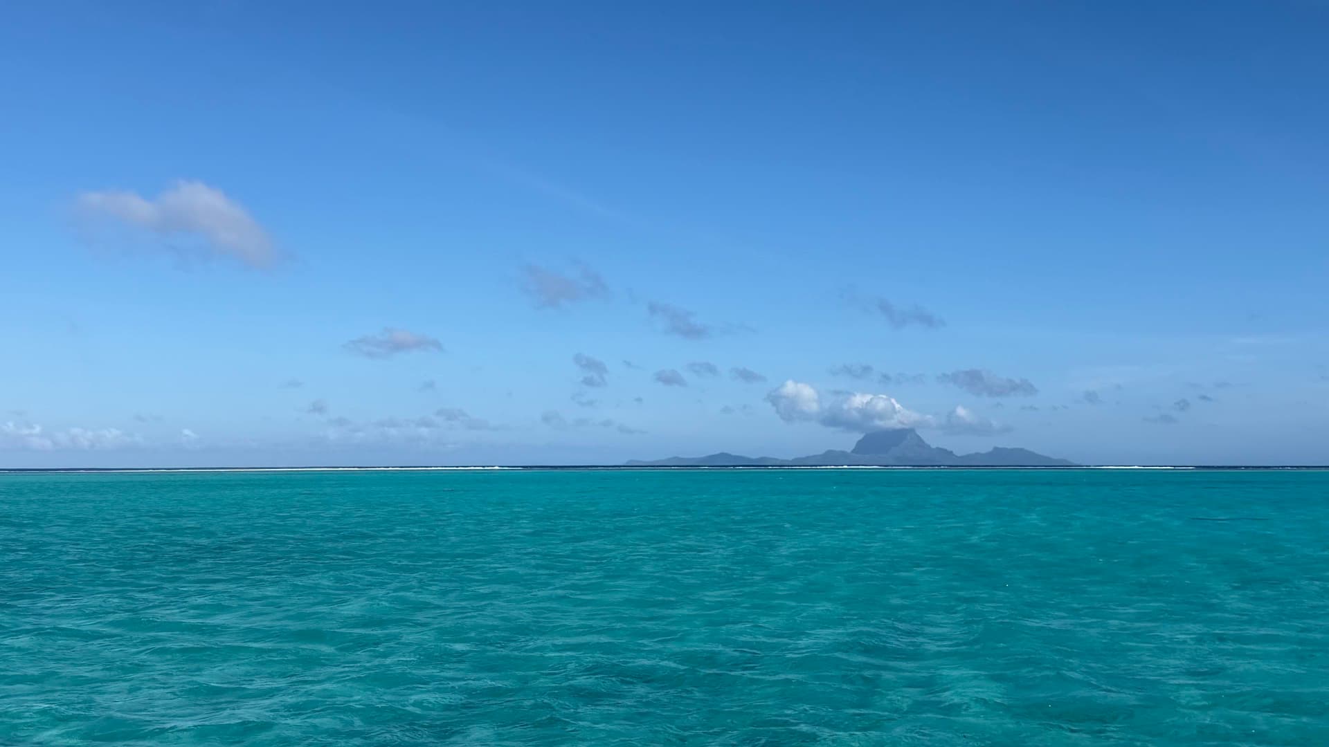 Bright turquoise ocean waters stretching toward a distant volcanic island under a blue sky