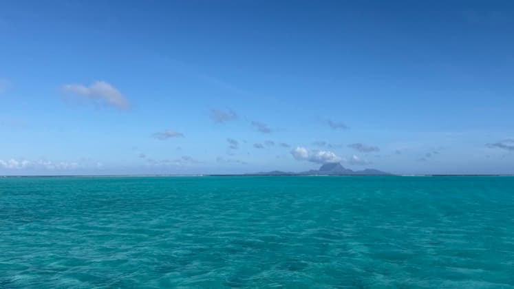 Bright turquoise ocean waters stretching toward a distant volcanic island under a blue sky