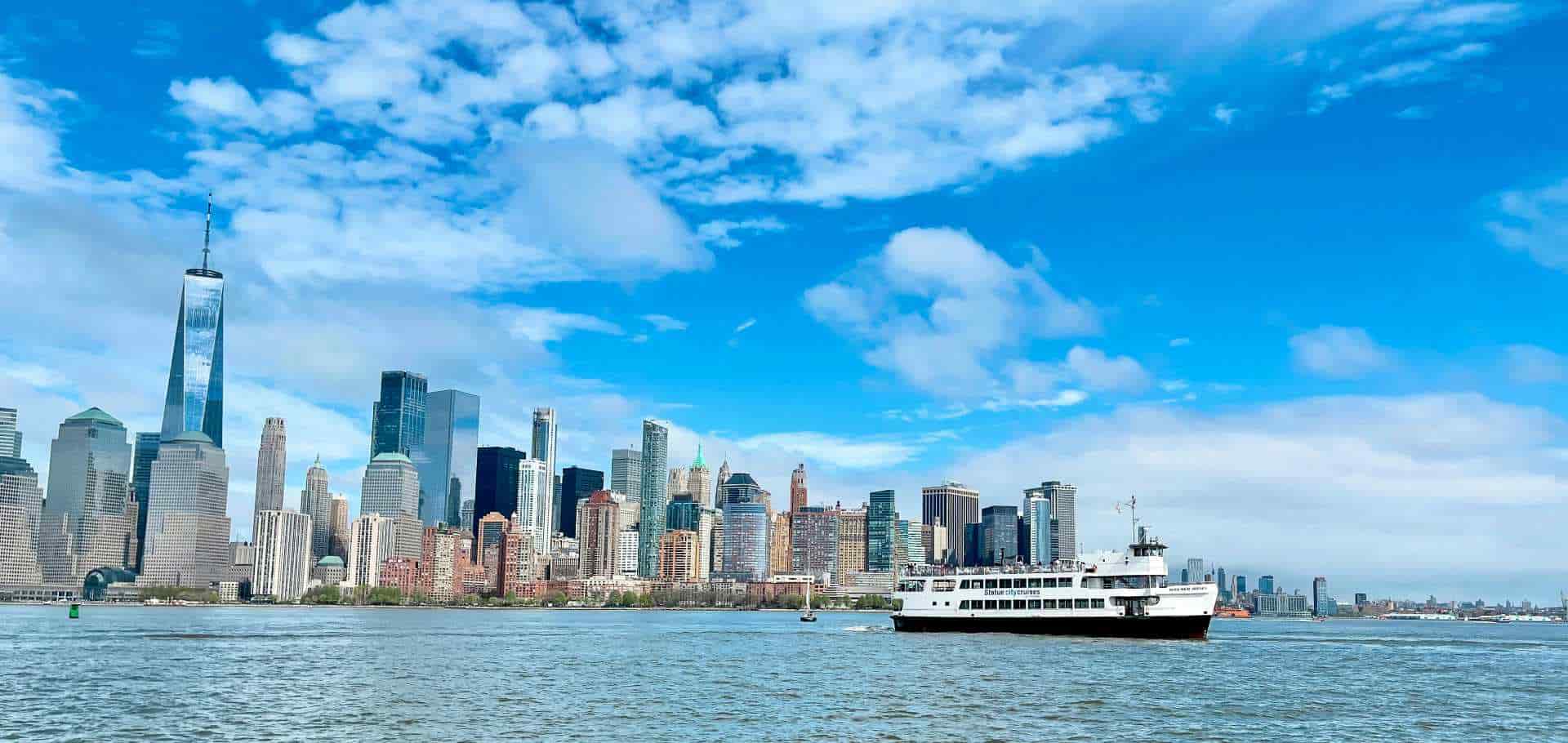 A passenger ferry cruises across New York Harbor with the Lower Manhattan skyline in the background
