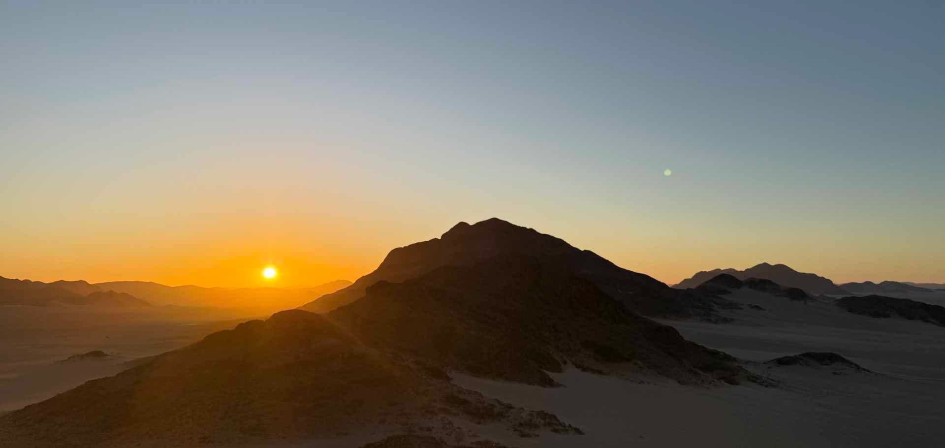 A vibrant golden sunset silhouetting rugged desert mountains and hills