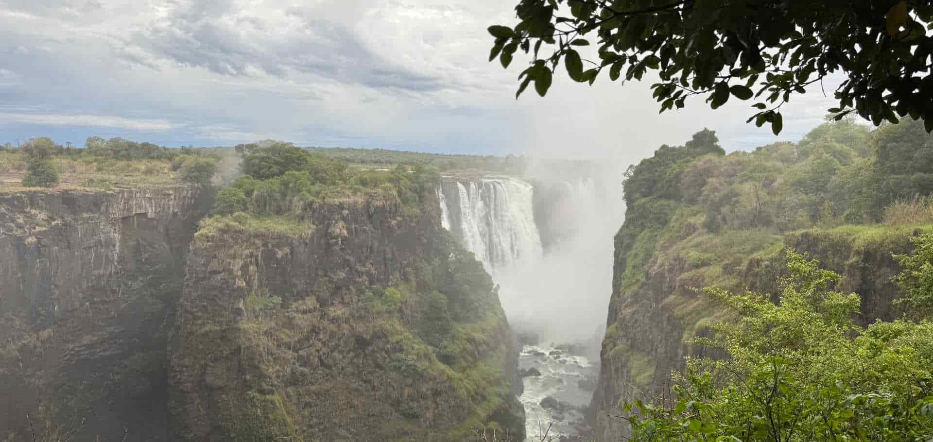 Lush vegetation frames the cascading waters and mist rising from Victoria Falls in Africa.