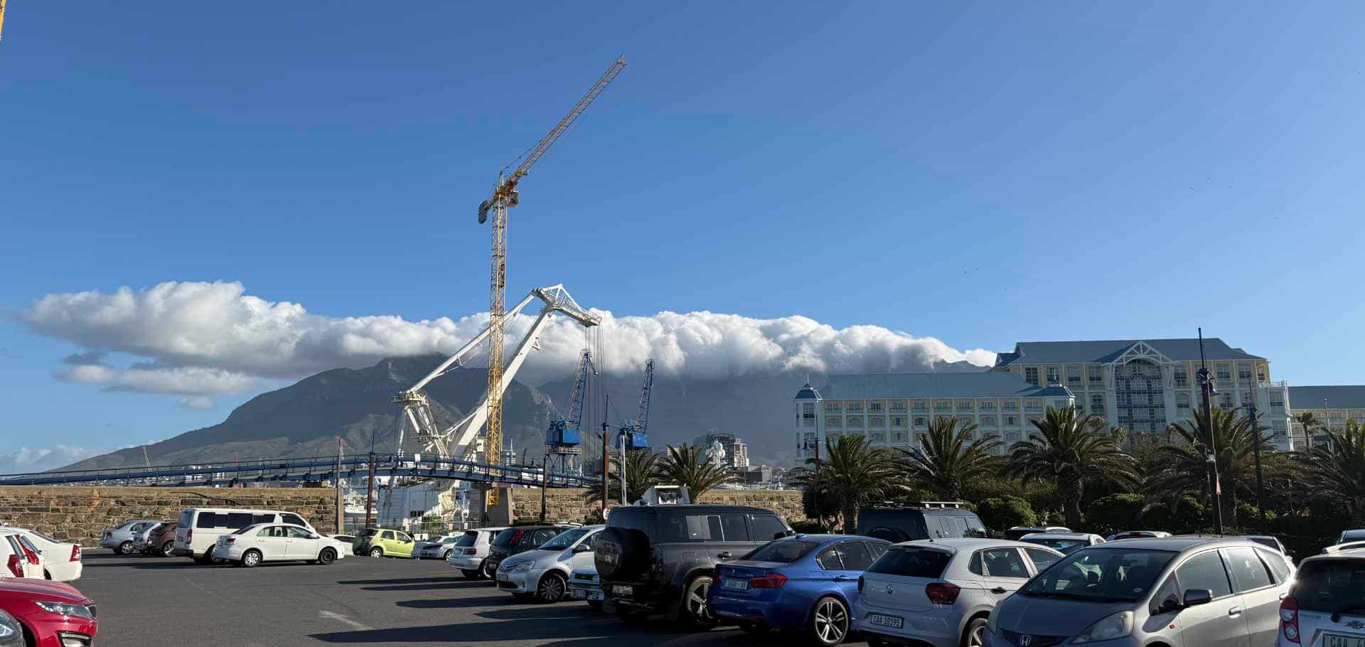 Industrial container cranes stand near vehicles and buildings under a cloudy mountain backdrop.