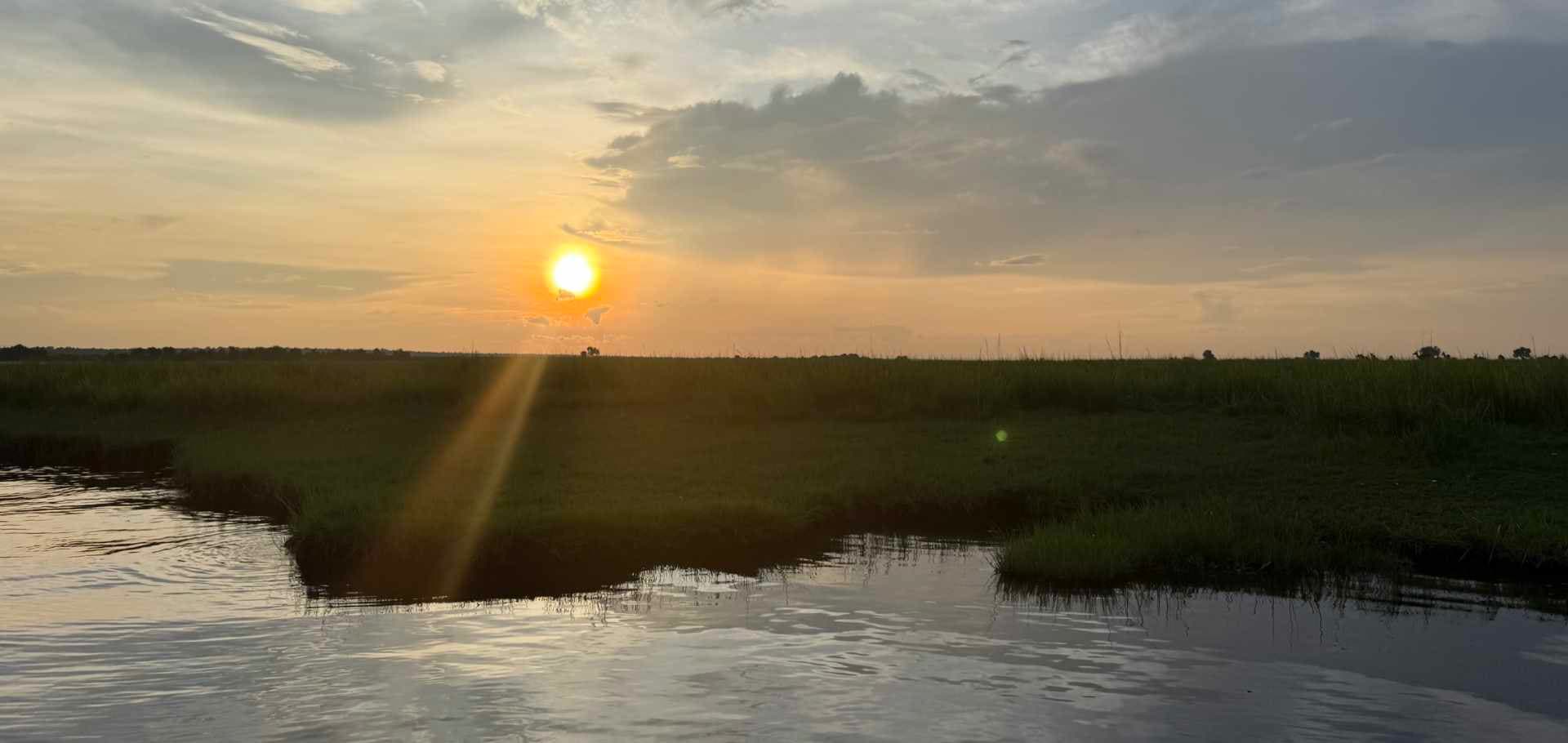 Golden sun setting over the calm waters and grassy floodplains of the Chobe River.