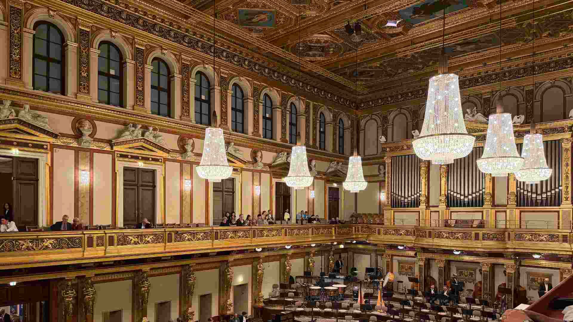 Lit chandeliers hang above the ornate balcony seating inside the golden concert hall.