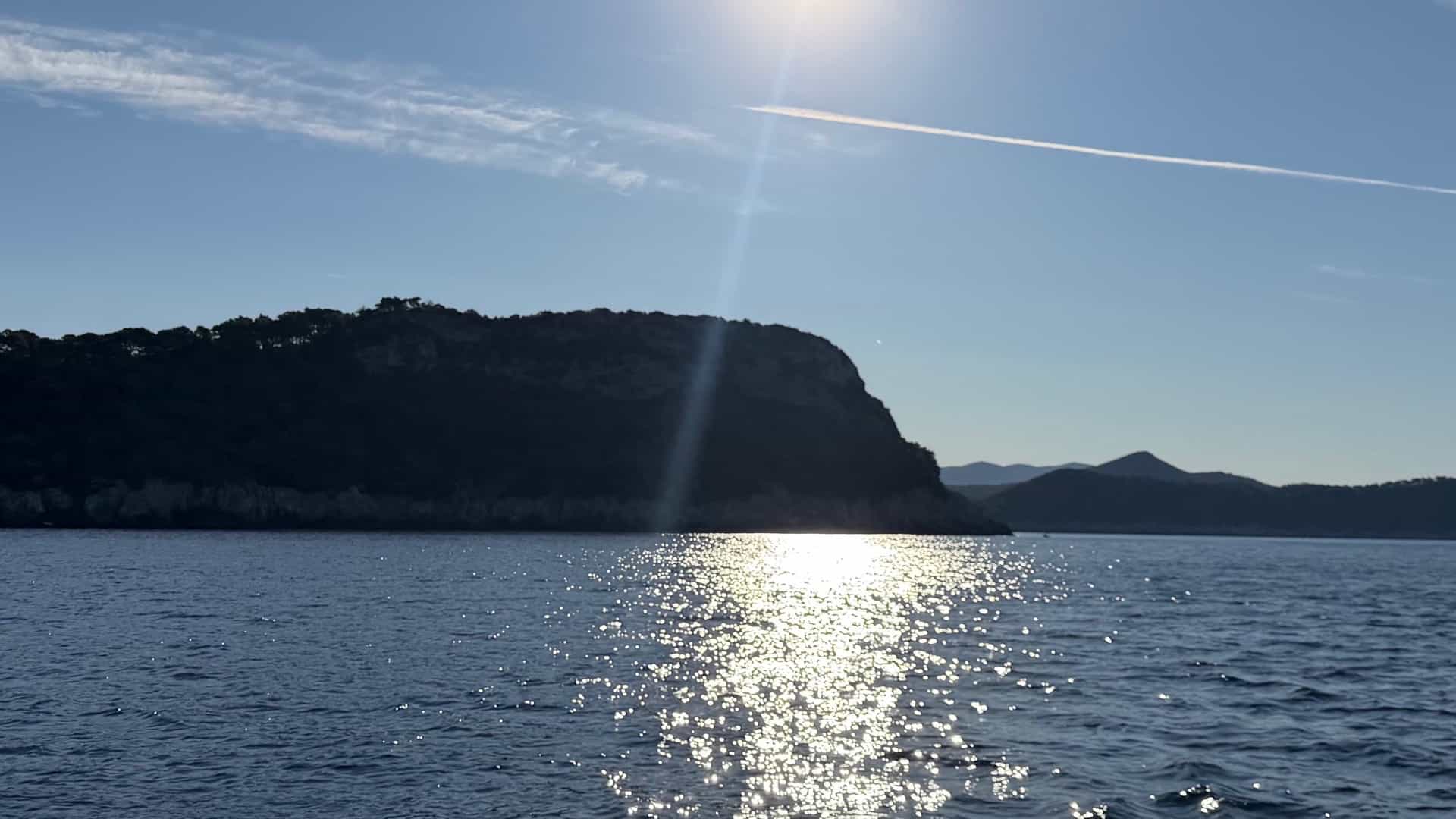 Sunlight glinting off dark sea waters near a forested coastal headland.