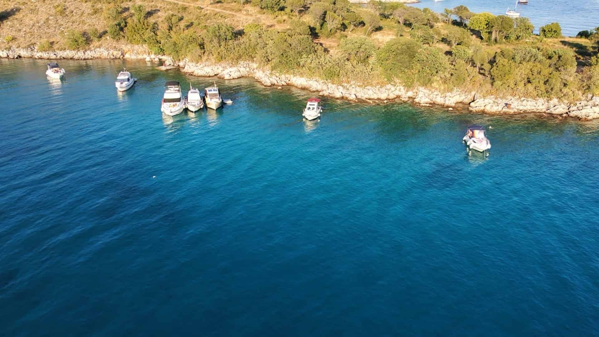 Modern monohull sailboat anchored in deep blue waters near the sunlit limestone coast of Sveti Juraj.
