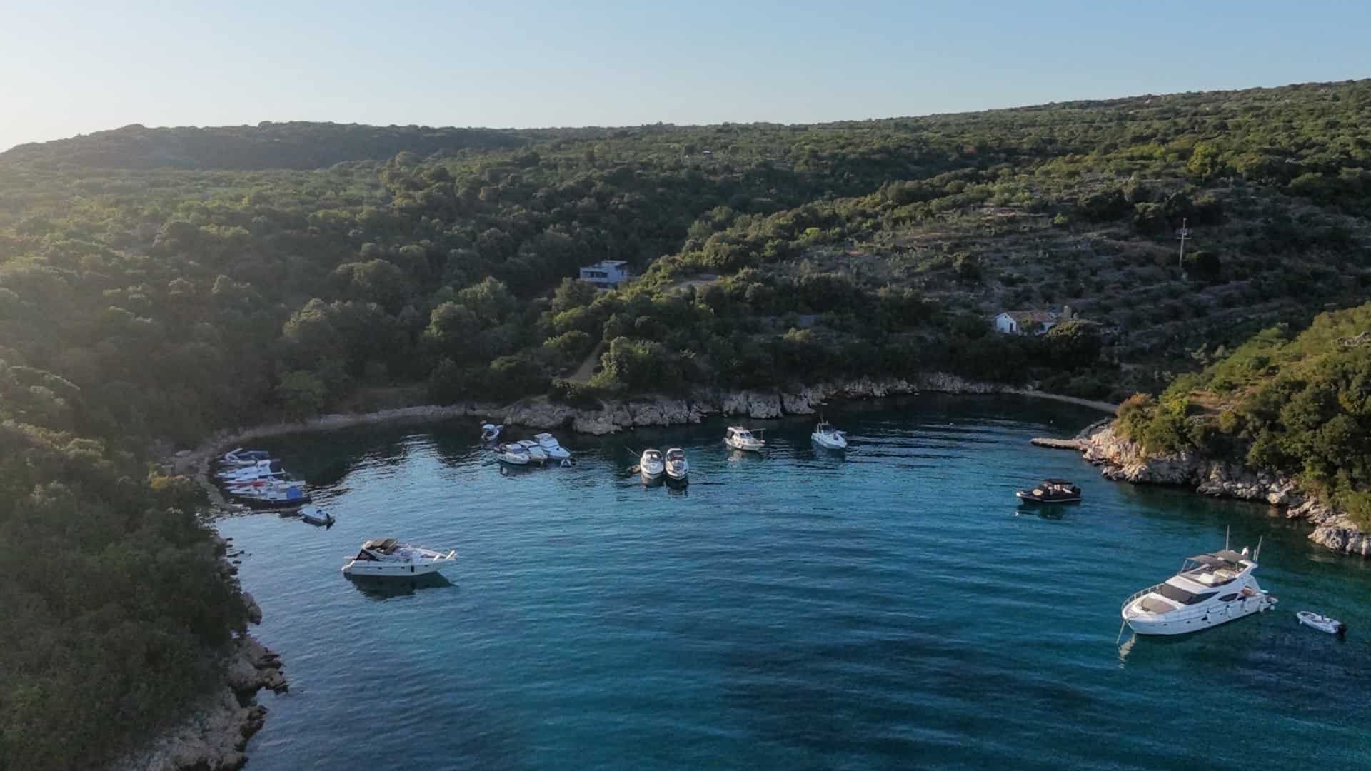 Sheltered bay surrounded by Mediterranean pine trees with yachts moored at dusk in Krk Island.
