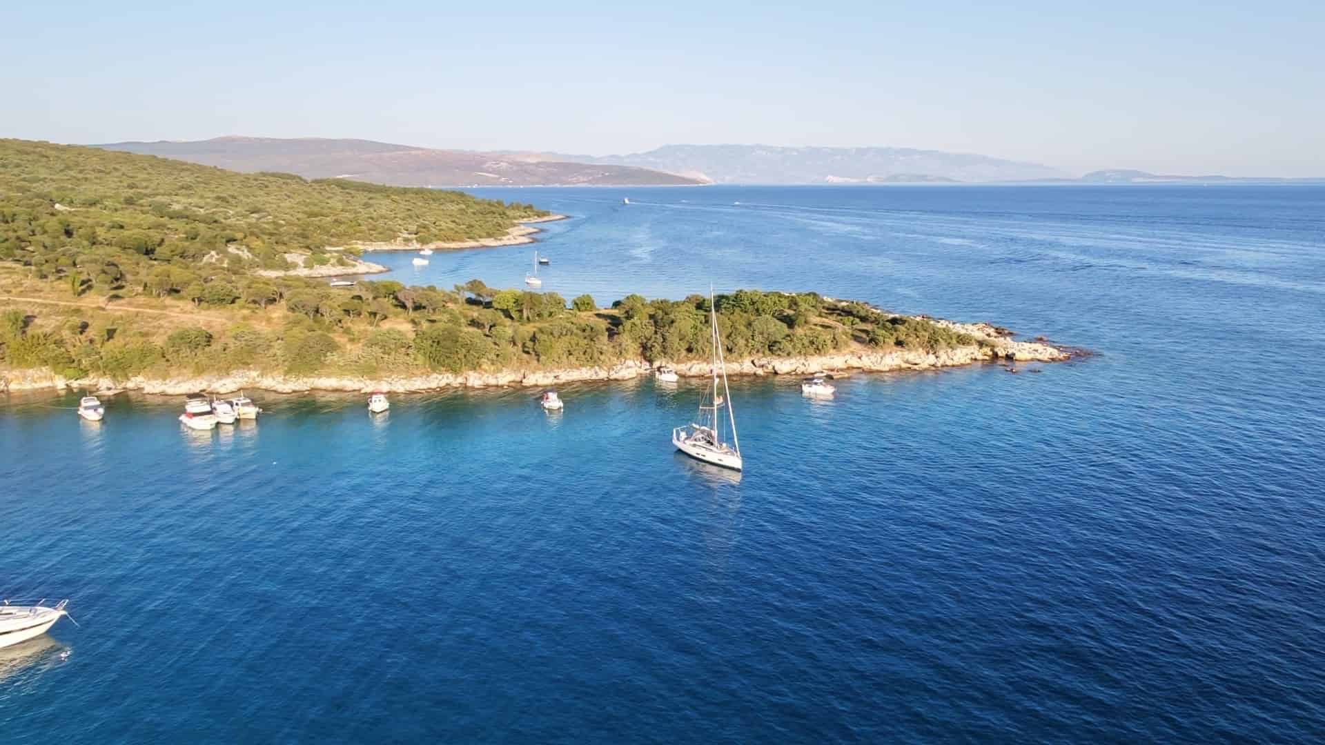 High-angle view of a sailboat anchoring off the forested headland of Krk Island facing the open Adriatic Sea.