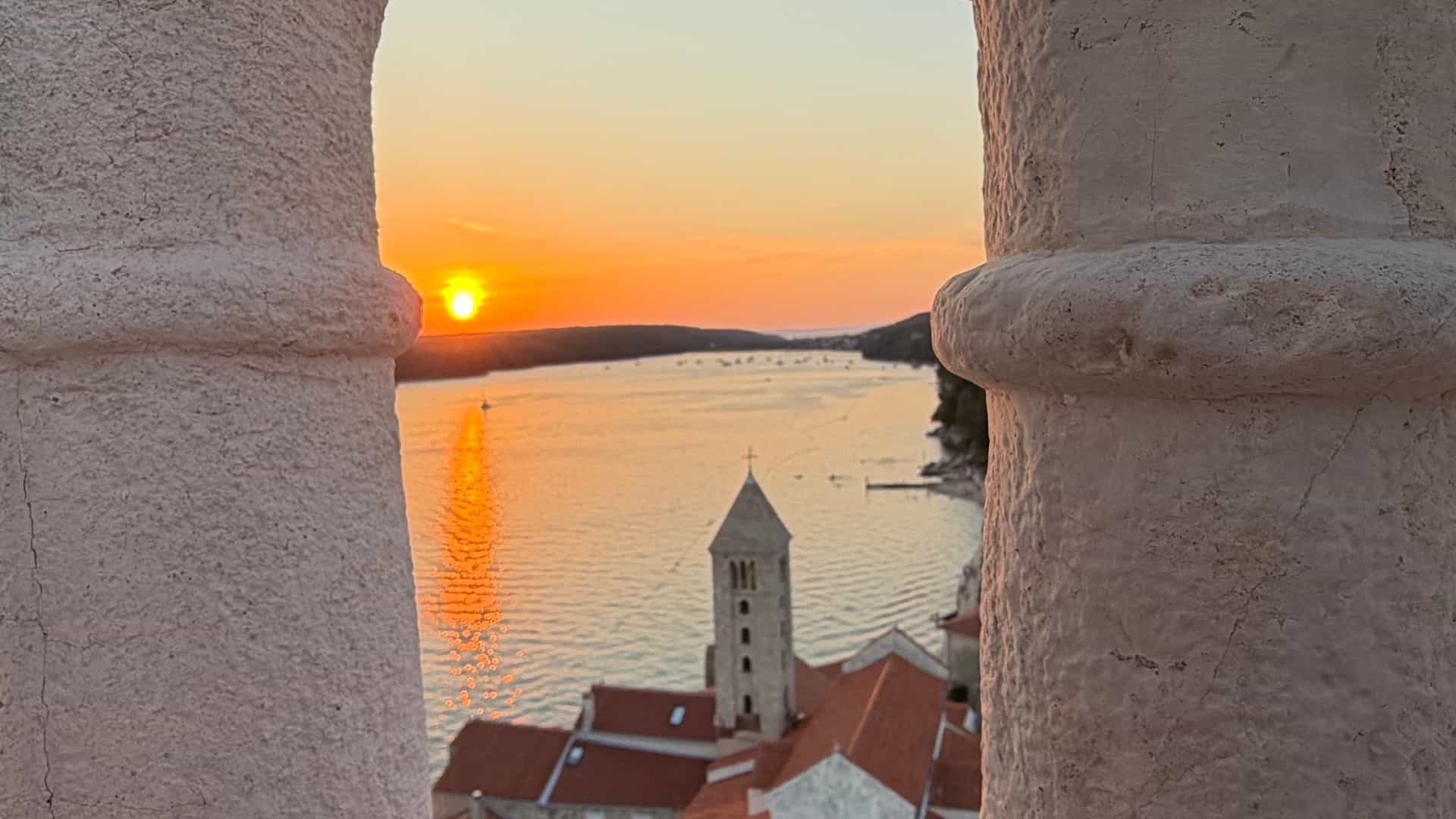 Sunset over the Adriatic Sea and church bell tower framed between stone bell tower arches.
