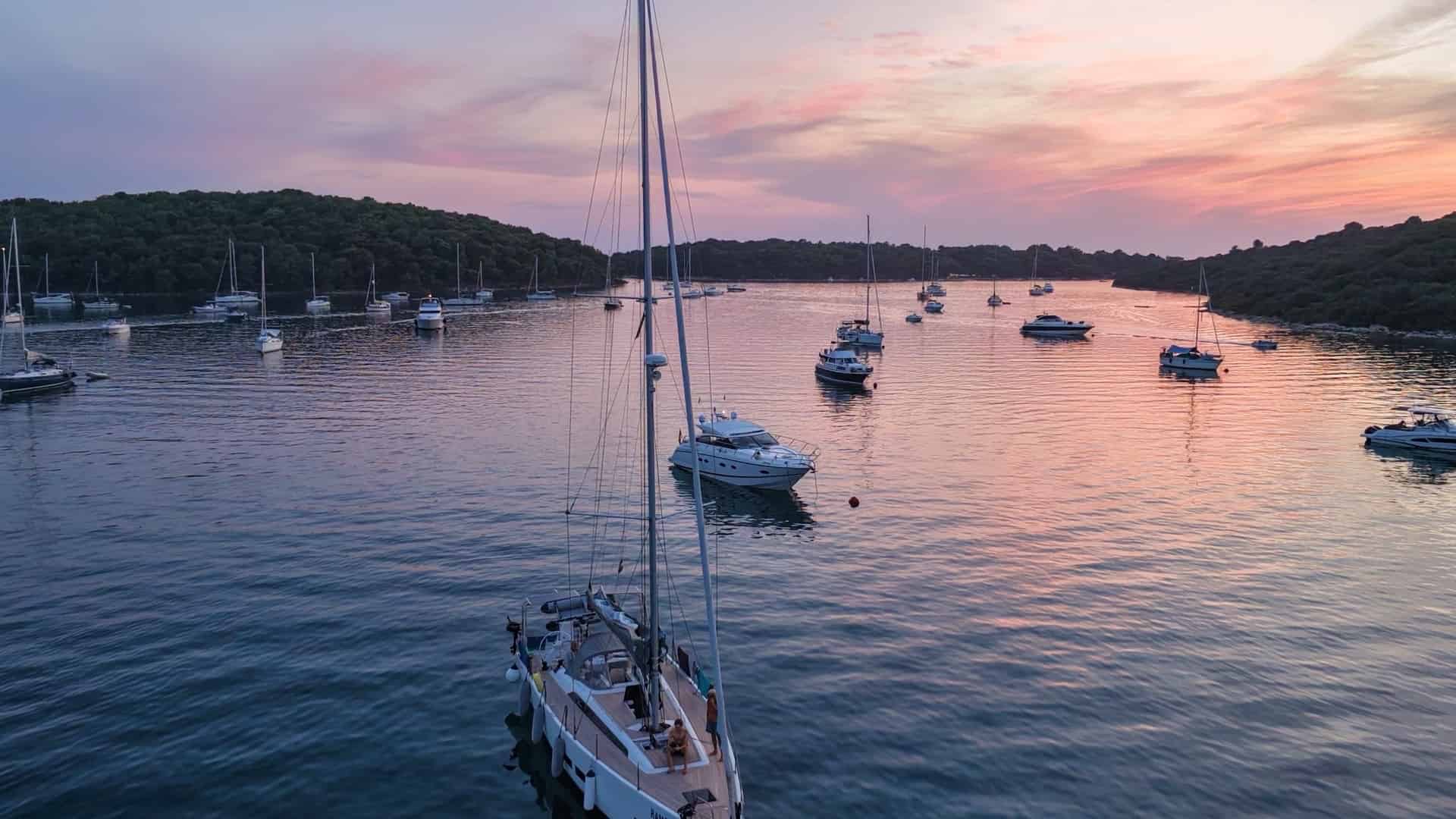 Tall sailing yacht anchored in the calm bay of Uvala Soline under vibrant twilight skies.