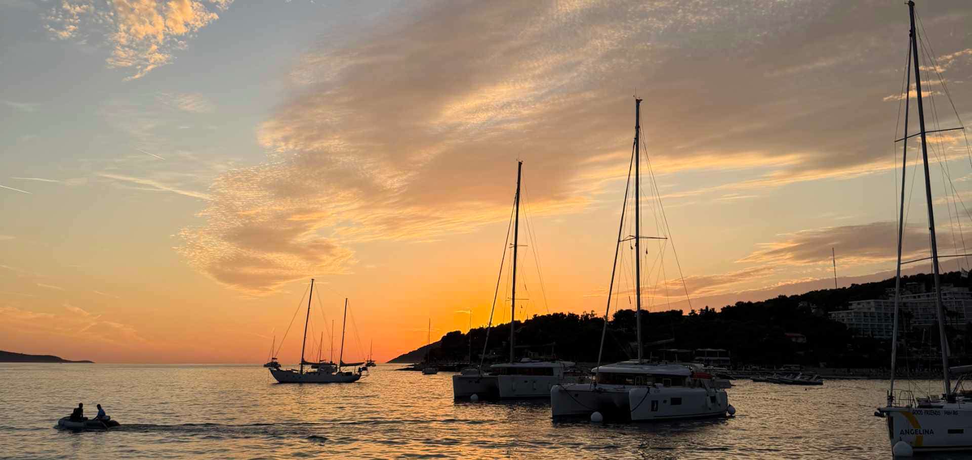 Sailboats anchored in a calm bay under a vibrant orange sunset sky