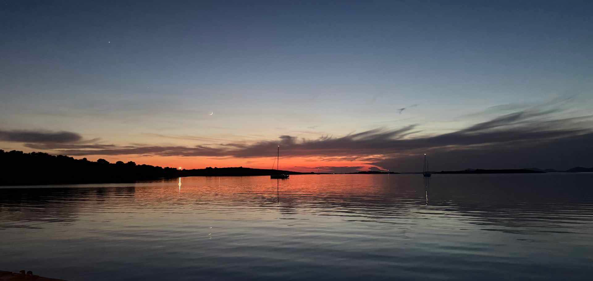 Tranquil evening seascape with a distant sailboat silhouetted against a red sunset