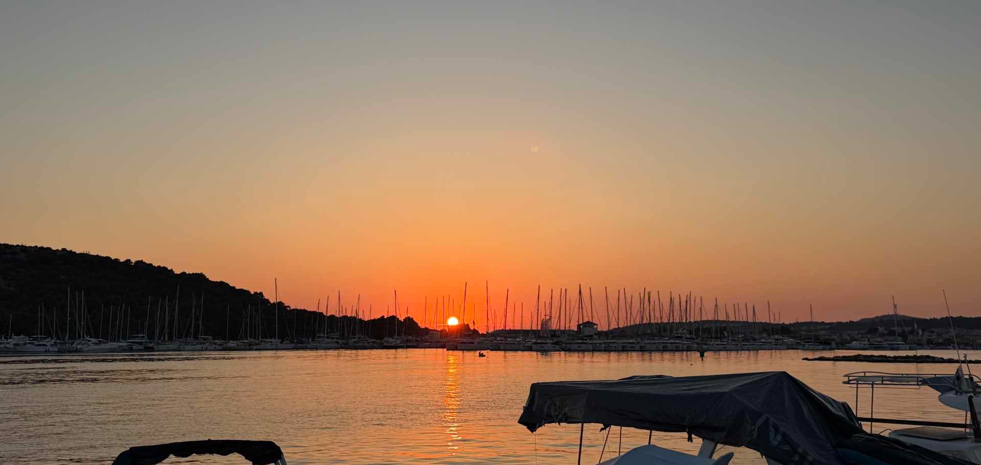 Tranquil evening seascape with a distant sailboat silhouetted against a red sunset