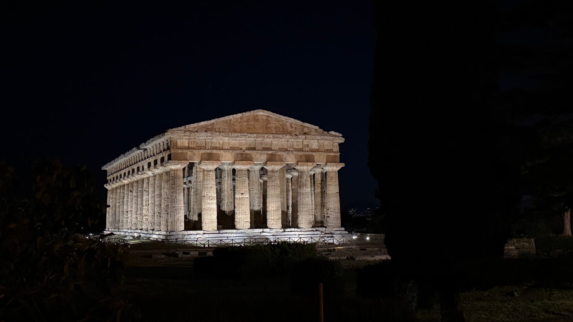 The illuminated Temple of Hera at Paestum glowing dramatically against the dark night sky.