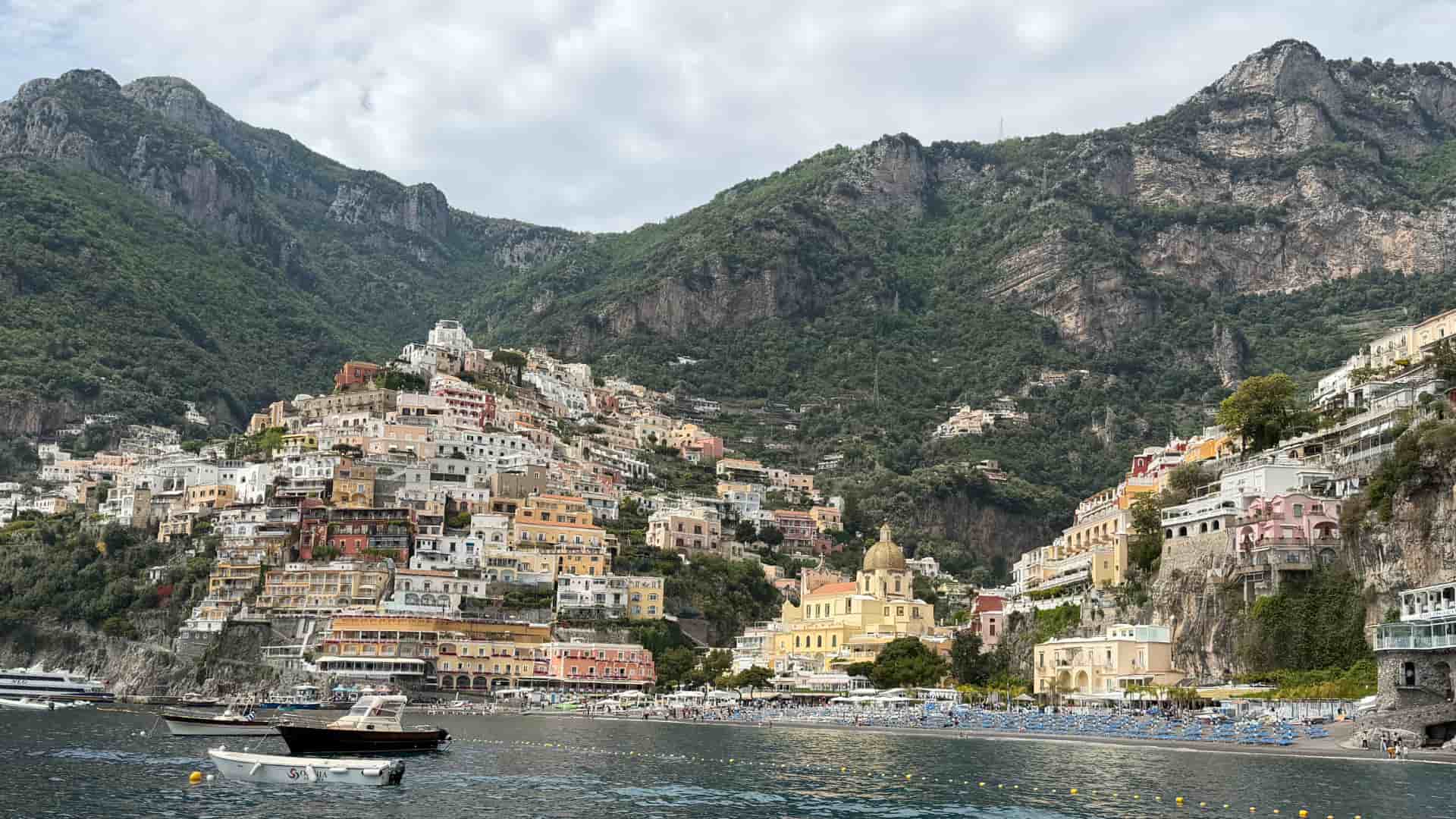 Colorful cliffside buildings and a bustling beach in Positano along the rugged Amalfi Coast.
