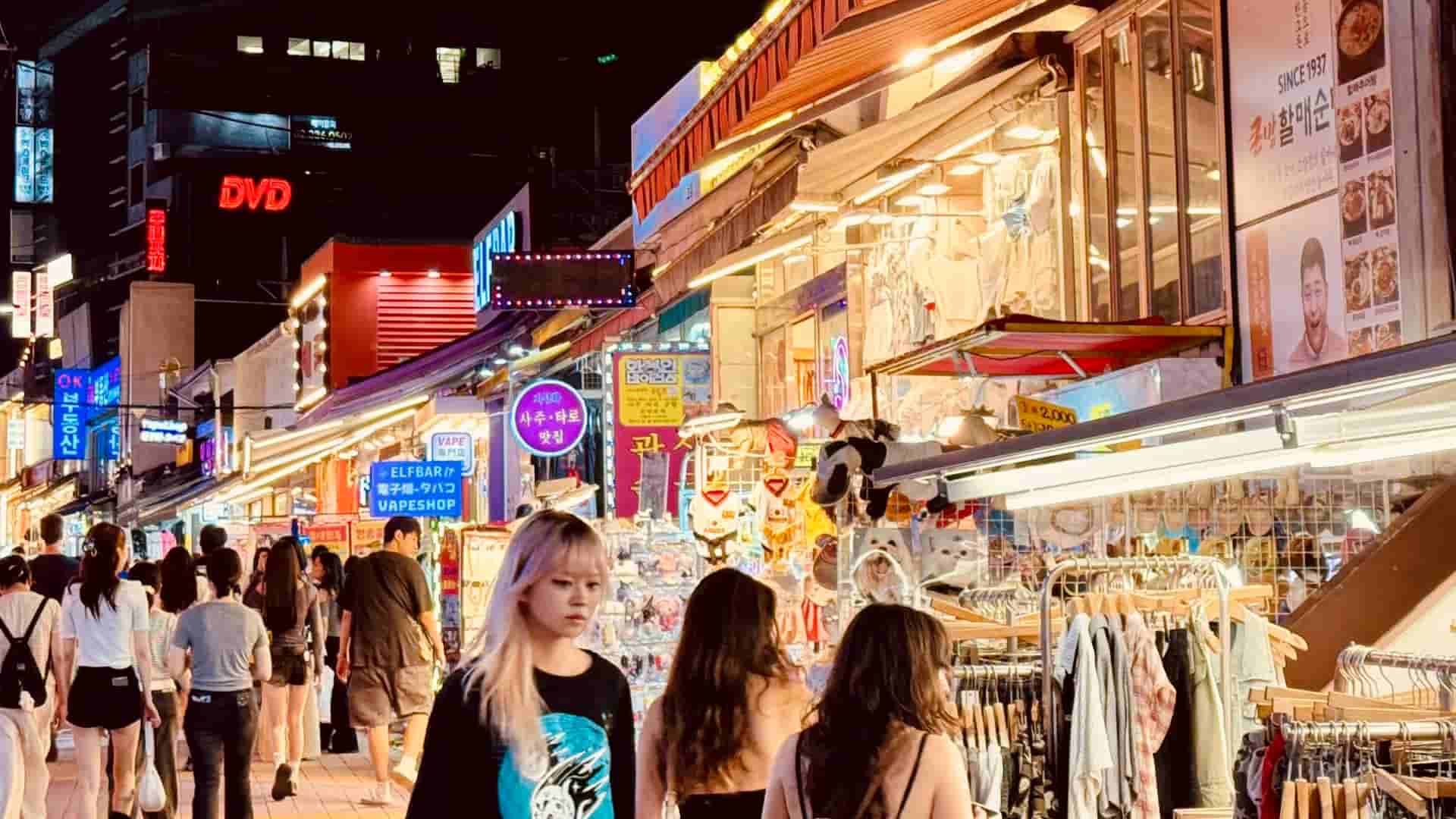 A lively, narrow nightlife alleyway packed with people and heavily illuminated by overlapping neon signs in both English and Korean, including a prominent marquee for Jack's Bar & Grill.