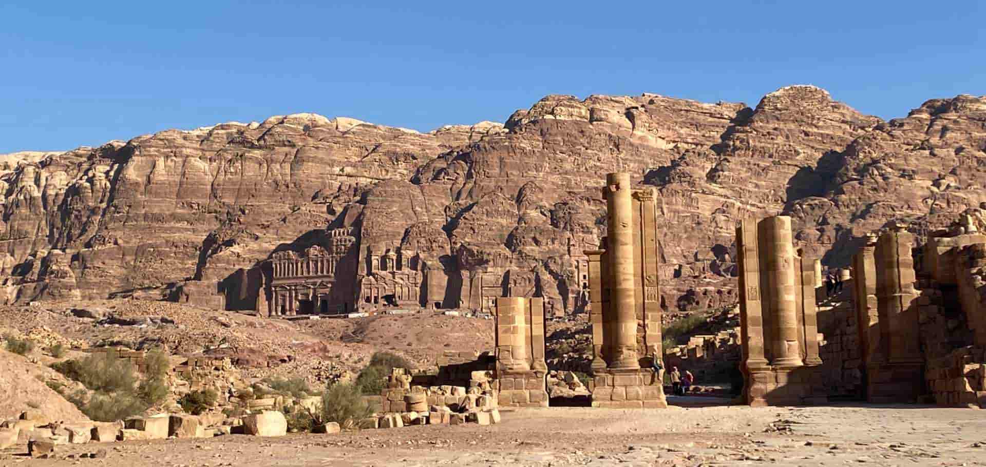 Ancient stone columns and weathered ruins standing against towering desert cliffs in Petra.