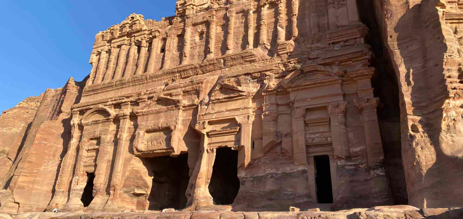 Intricate stone carvings and towering pillars cut into the pink sandstone cliff face in Petra.